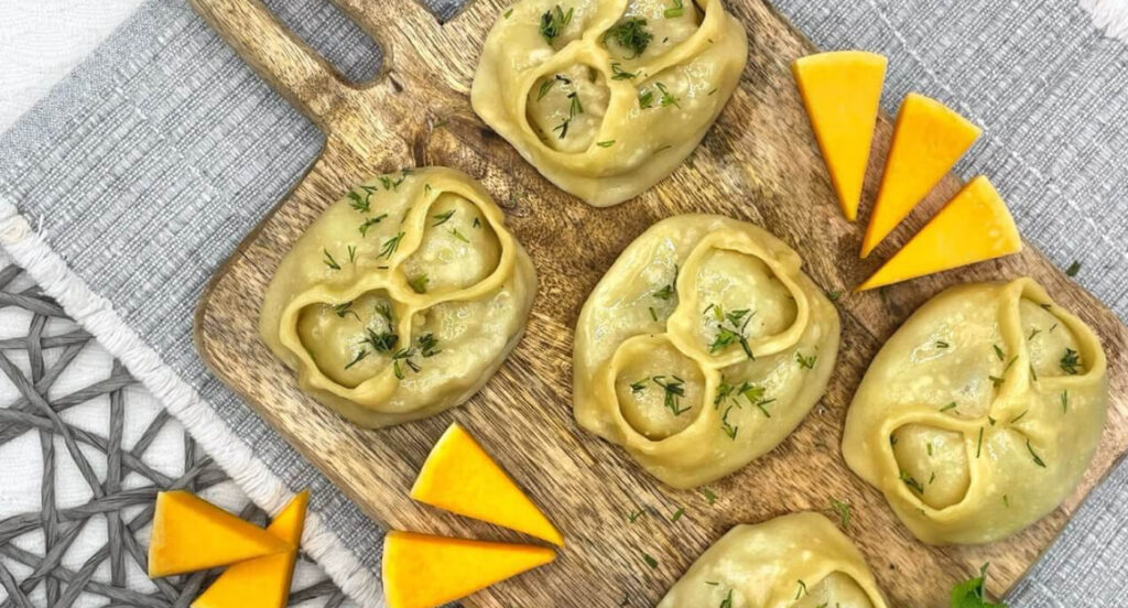 Манты с рубленной бараниной и тыквой на деревянной дощечке, украшенные кусочками сыра