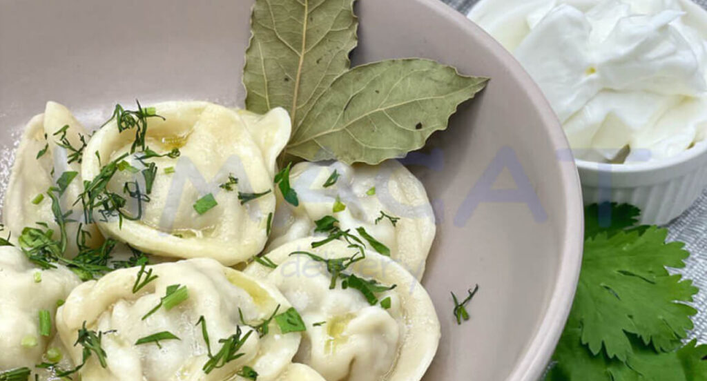 Пельмени со свининой и говядиной на тарелке, украшенные лавровым листом и зеленью