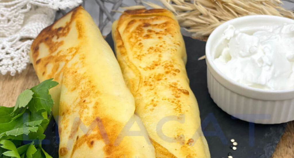 Два блина с мясом и яйцом на темной тарелке, украшенные петрушкой и сметаной