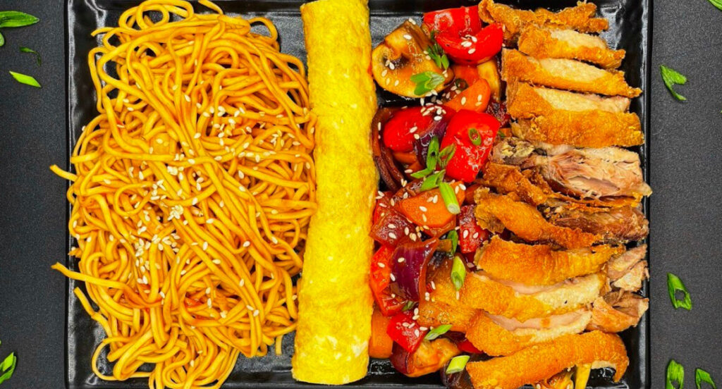 Хрустящая утка, цукини, морковь, сладкий перец, красный лук, грибы, ананас, зеленый лук, соус и кунжутные семечки сверху, омлет.